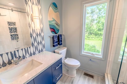 A wide angle photo graph of a newly remodeled bathroom with blue cabinets and coastal interior design elements