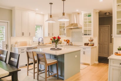 Wide angle photo of a kitchen and dining room with pastel blue cabinetry and a bouquet of roses on the island