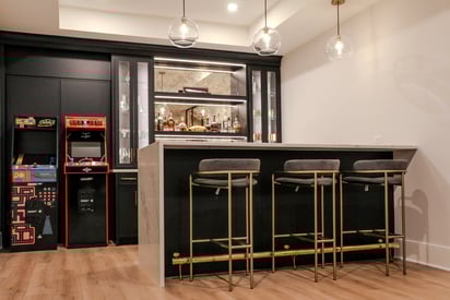 Full home bar with 3 bar stool chairs and two arcade cabinets next to the bar