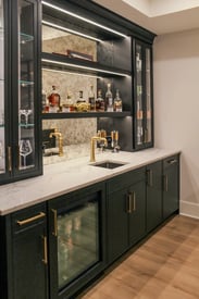 Close up of the back of a home bar with bottles of alcohol sitting on the black shelves