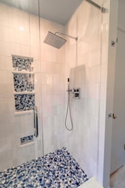 Walk in shower with embedded shelving, a rainfall shower head, and a decorative tile floor pattern that is blue and white