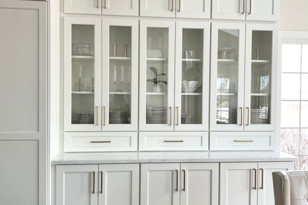 White kitchen cabinets with glass pane cabinet doors and silver stainless steel trim