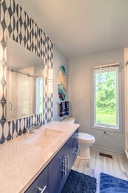 Narrow angle of a single vanity bathroom remodel with the toilet in the background and the mirror with two wall scones on the left wall