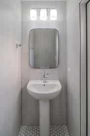 Close up photo of a private powder room washbasin with hard white LED lights and a mirror