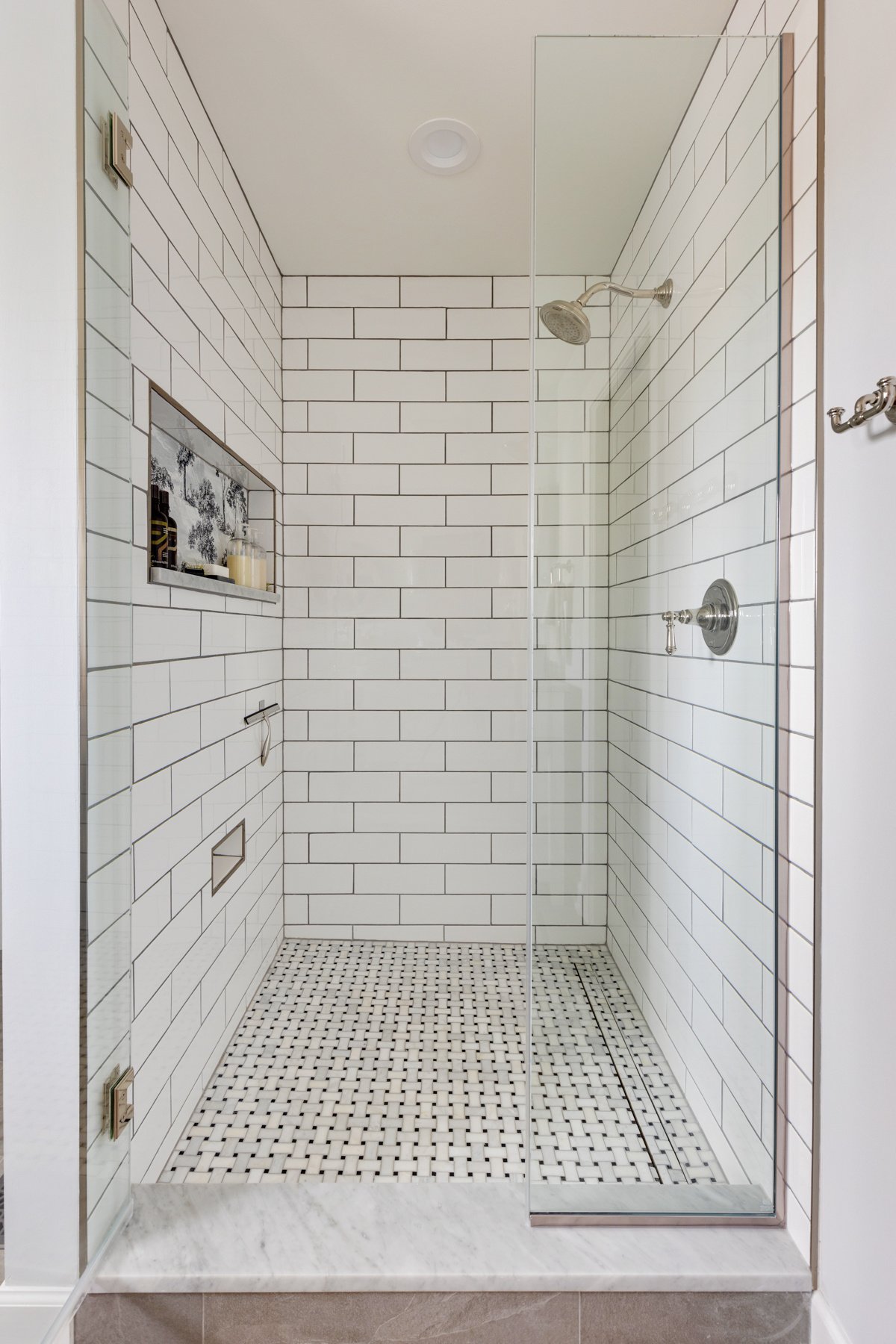 Full view of shower area. Tiled walls, shower niche and floor, glass doors and stainless steel rainhead