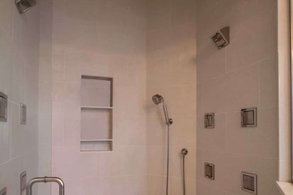 warmly lit shower with multiple jets for water and an embedded storage shelf for shampoo, conditioner, and body wash