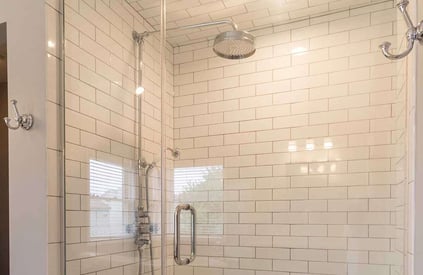 Walk in shower with a rainfall showerhead, glass shower door, and white tile walls