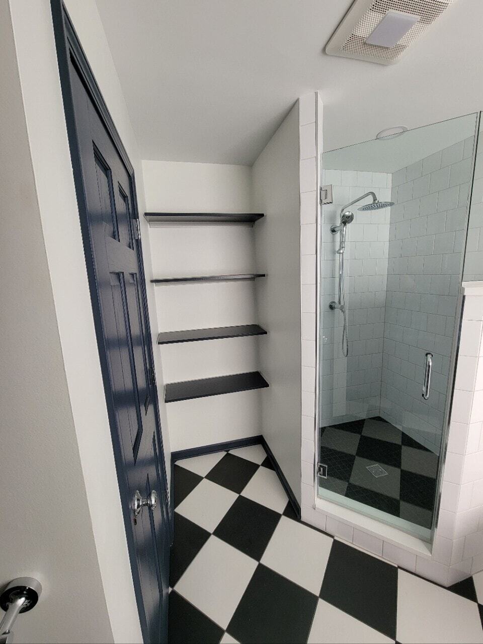 Small bathroom corner shower with black and white checked tile and rain showerhead