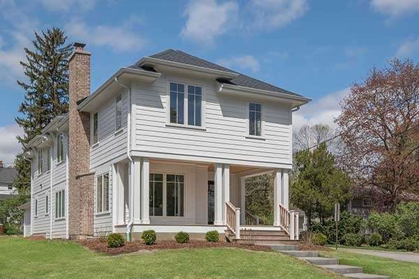 Exterior photo of a two story home with a porch to walk out on, lots of tall and narrow windows, and a chimney made of brick on the left side of the home