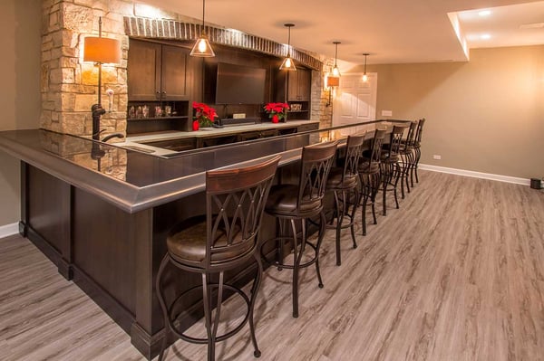 luxurious and warm basement wet bar with pendant lights and high-boy bar chairs