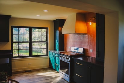 Wide angle photo of a kitchen stove with decorative tile backsplash and an exhaust hood