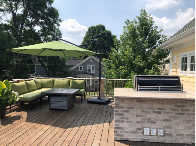 Outdoor living space with green umbrella and green sectional couch and a mini outdoor kitchen with a grill