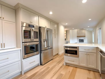 Wide angle photo of a kitchen remodel with built in dual over and fridge stainless steel appliances