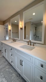 A double vanity bathroom with two mirrors, wall scones for lighting, and white cabinetry/countertops