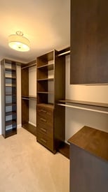 Master bedroom closet with a soft white lamp overhead and lots of embedded shelving for folded clothes