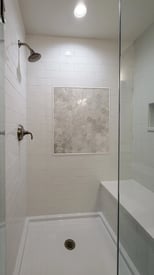 Spacious and accessible walk in shower with black finishes, white tile, and overhead lighting