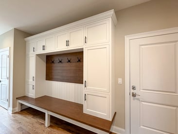 Functional and elegant coat closet with white cabinetry and a dark wood bench