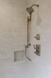 Another shower in a guest bathroom with luxurious cream tile walls, built in shelving, and silver fixtures