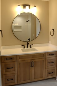 A powder room with a single vanity, one large round mirror, and an over head wall scone for lighting