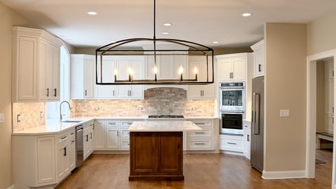 A new home build kitchen with decorative lighting fixtures, white cabinetry, and a beautiful backsplash