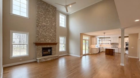 A spacious living room with a vaulted ceiling, stone fire fireplace, and wood flooring