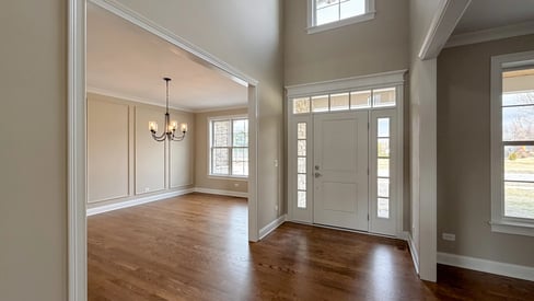 A spacious and luxurious front entrance to a new home build with an elegant front door, a chandelier in the background, and lots of natural light