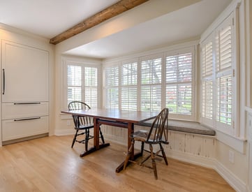 Two person dining table in front of a bumped out window with a reading bench