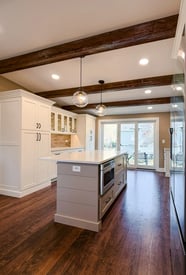 Wide angle of a kitchen remodel with exposed support beams and embedded can lighting