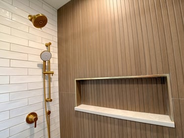 Close up of shower built in shelf and gold fixtures/finishes