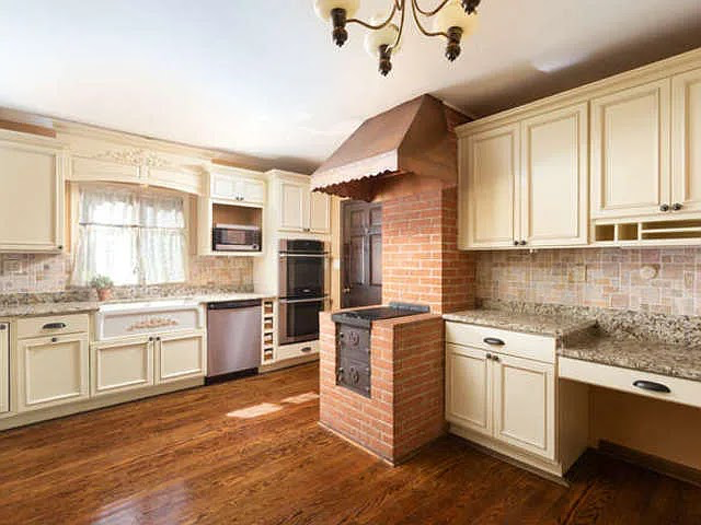 A before picture of a kitchen with ivory cabinets and granite countertops, an old wood burning stove and copper hood.