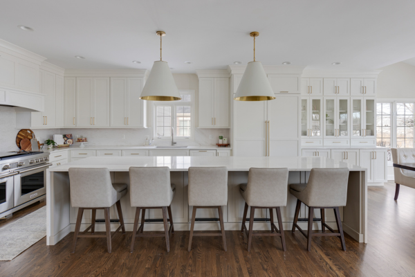 All white kitchen with wood floors and an extra Long Island, featuring cascading quartz countertops with gold and white conical pendants.