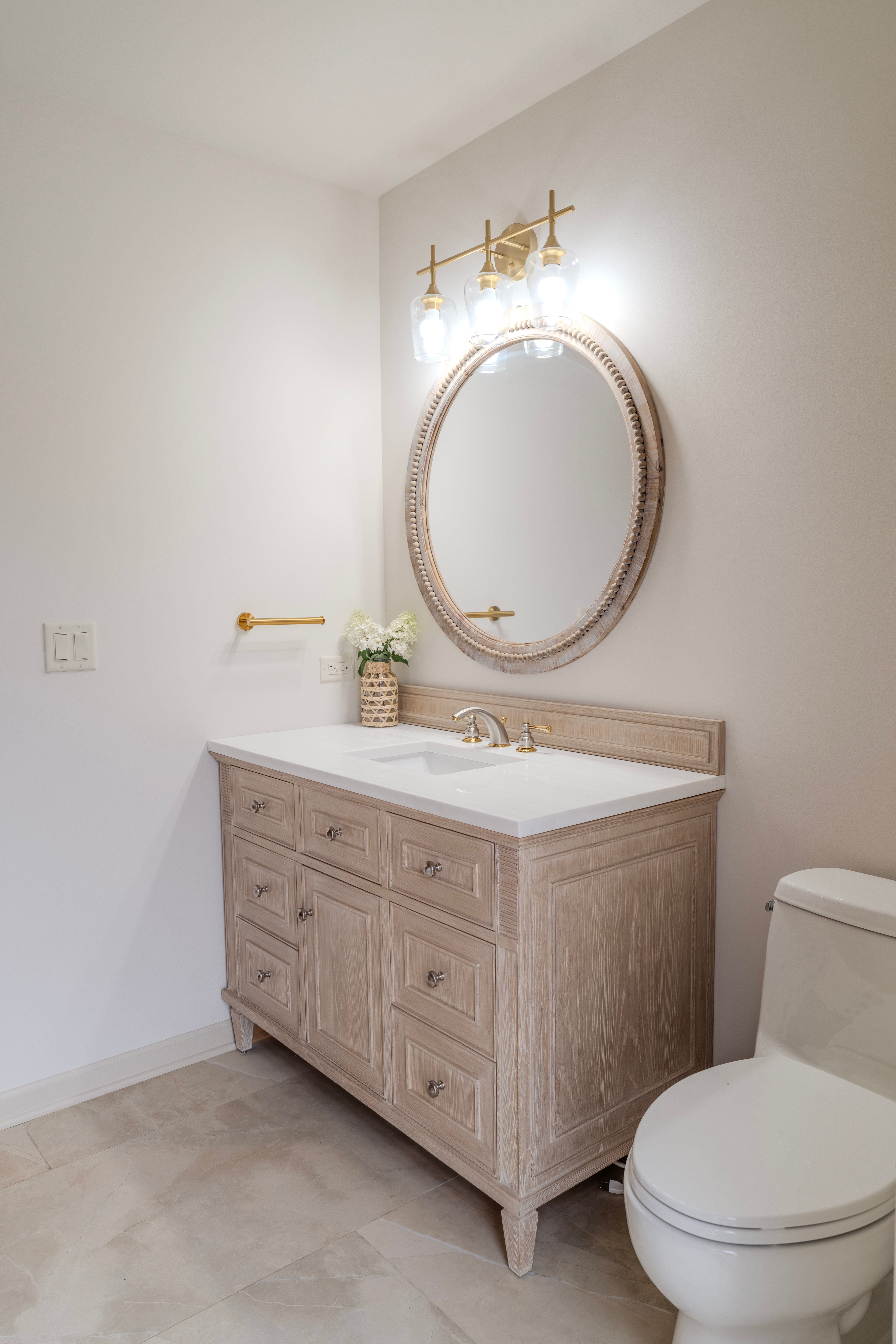 Power room remodel with a single vanity, coastal wood color, a large round mirror, and brushed gold finishes.